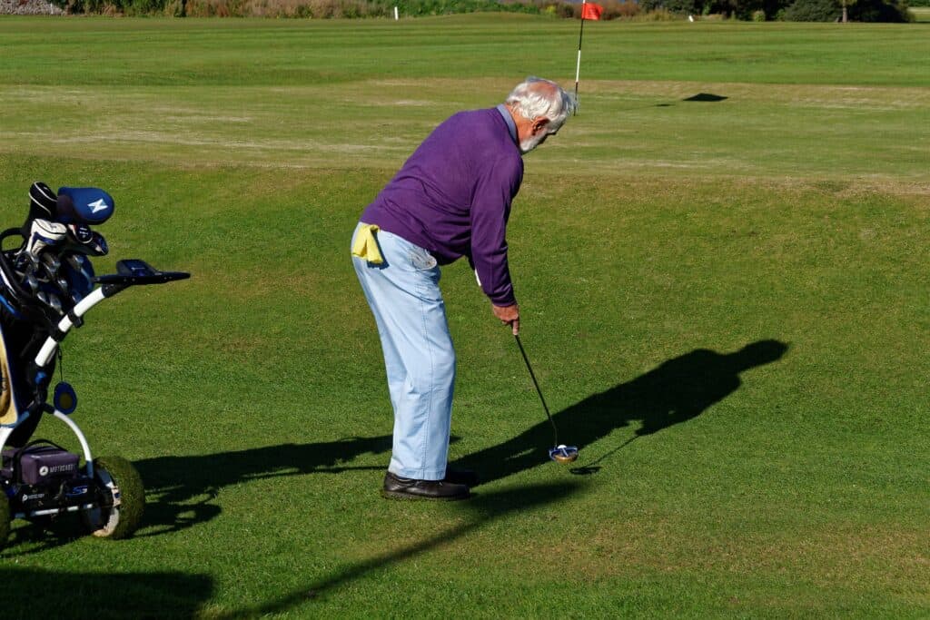 An elderly man preparing to hit a golf ball on a golf lawn